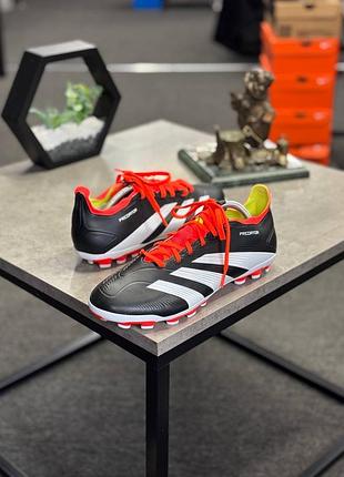 Футбольні бутси adidas predator 24 league low, що відрізняються яскраво-червоними шнурками та білими смугами на чорному фоні.