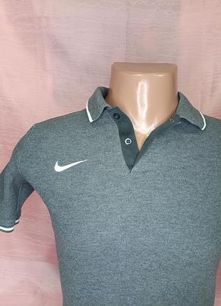 На изображении представлено серое,подростковое поло nike team club 19 с белым логотипом swoosh и контрастной окантовкой на воротнике и рукавах.
