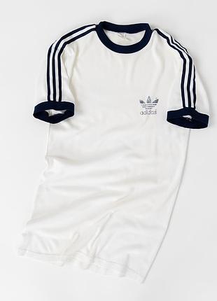Класична, вінтажна футболка adidas у стилі 70–80-х років. виконана в білому кольорі з темно-синіми, контрастними манжетами, коміром та легендарними