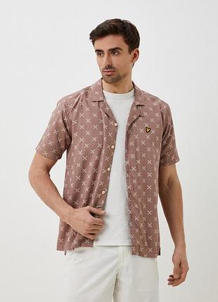 Чоловіча сорочка lyle & scott ніжно-рожевого кольору з принтом у вигляді хрестиків та фірмовою, вишитою емблемою на грудях. модель має комір camp
