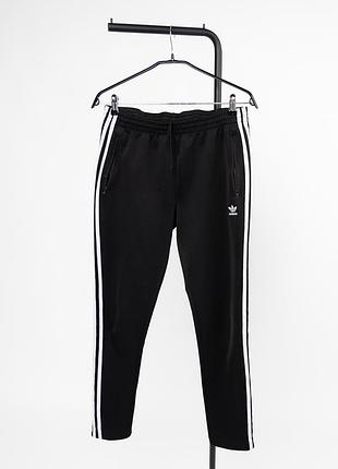 Жіночі, спортивні штани adidas чорного кольору з культовими трьома білими смужками вздовж боків. модель має еластичний пояс зі шнурком для
