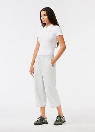 Жіночі, спортивні штани lacoste sport світло-сірого кольору довжиною 3/4. модель має еластичний пояс зі шнурком для регулювання посадки, дві бічні киш