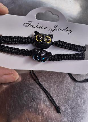 Набор парных браслетов "fashion jewelry" имеет черные плетеные шнурки и шармы в виде черных котов с глазами разных цветов.
