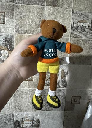 Ші                    на фото зображено плюшевого ведмедика в зеленому худі з написом «scotland is cool» та жовтих шортах.