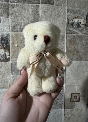 Невеликий плюшевий ведмедик із кремовим хутром та декоративною стрічкою з написами «teddy bear