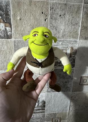 Плюшеву іграшку персонажа шрека (dreamworks) у його класичному вбранні з коричневим жилетом та рудими штанами
