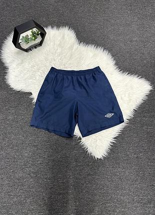 Темно-сині спортивні шорти від umbro вирізняються легким матеріалом з поліестеру та білим вишитим логотипом у вигляді ромба на штанині.