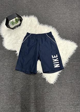 Темно-сині нейлонові спортивні шорти nike з білим вертикальним логотипом на штанині та білим кантом на кишенях.