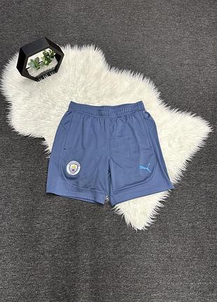 Сині тренувальні шорти puma manchester city (сезон 2024/25), прикрашені емблемою клубу та логотипом бренду.