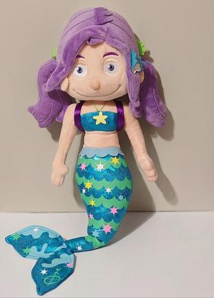 Мягкая игрушка-русалка бренда melody mermaid имеет характерный хвост с блестящим узором в виде чешуи и звезд.