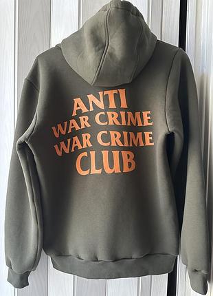 Худі оливкового кольору з надписом « anti war war crime club помаранчевого кольору на спині.