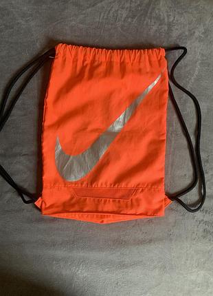 Помаранчевий рюкзак-мішок — модель nike fb gymsack 3.0, відома своїм великим сріблястим логотипом swoosh.