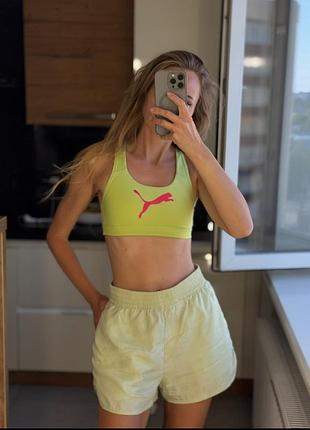Спортивный топ puma 4keeps выполнен в ярком лаймовом цвете с контрастным розовым логотипом