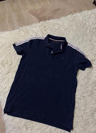 Темно-синее поло от tommy hilfiger, украшенное фирменной брендированной лентой на плечах и рукавах.
