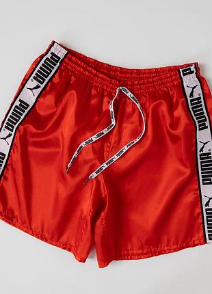 Яскраві, чоловічі шорти puma червоного кольору з фірмовими стрічками з логотипами по боках. модель має еластичний пояс зі шнурком для регулювання