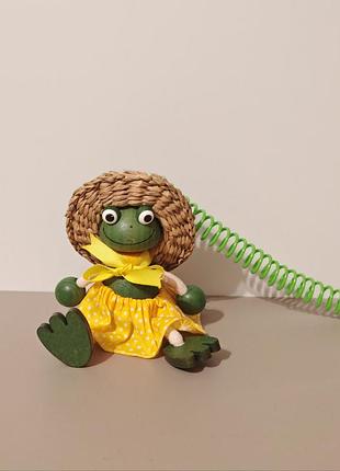 Декоративная подвесная игрушка-пружинка (bouncy wooden puppet / jumpie) в виде лягушки в соломенной шляпке и жёлтом платьице.