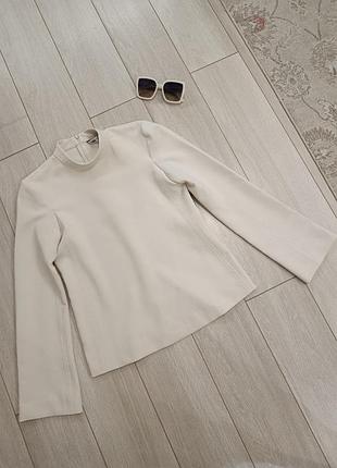 Мінімалістична блуза світло-бежевого (екрю) кольору від бренду zara. вона має високий комір-стійку та довгі розкльошені рукави вільного крою