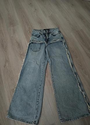 Широкі світло-блакитні джинси вільного крою (baggy/wide-leg) з необробленими декоративними краями.