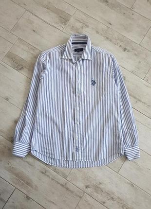 Класична  сорочка в синьо-білу смужку від u.s. polo assn. доповнена фірмовою вишивкою логотипа на грудях.