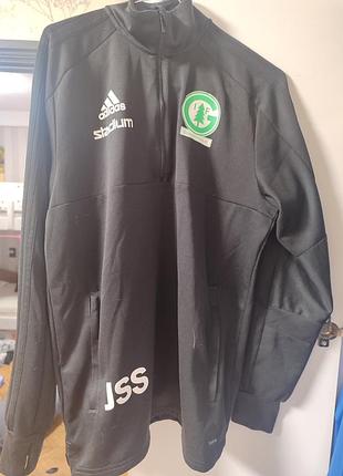 Это черная тренировочная кофта adidas gransholms stird на молнии до середины груди, имеющая зеленую эмблему клуба.