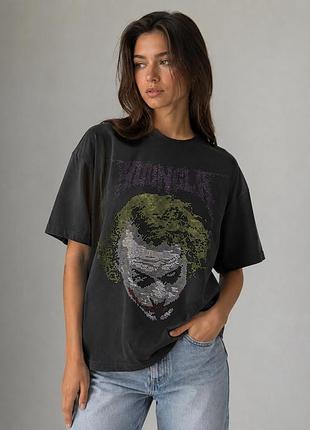 Представлена ​​чорна оверсайз-футболка х модель joker) із колаборації з dc comics за мотивами трилогії «темний лицар», прикрашена стразами .