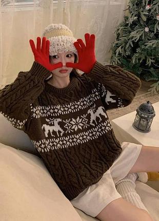 Свитер коричневого цвета, с косами, украшен силуэтами оленей и снежинок.
