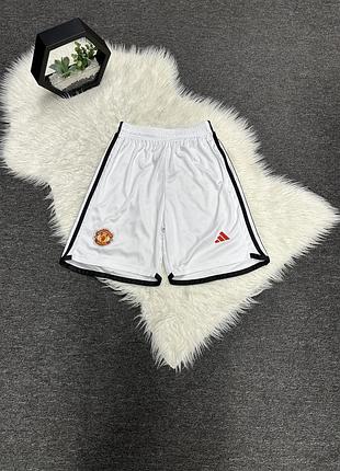 Футбольні шорти adidas manchester united (сезону 23/24) з червоним логотипом бренду та емблемою клубу.