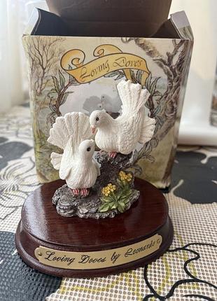 Витончена статуетка "loving doves by leonardo" зображує двох ніжних білих голубів, які сидять на гілці дерева серед жовтих квітів.