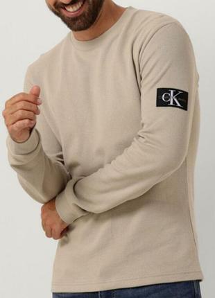 Бежевый хлопковый лонгслив свитшот calvin klein jeans фактурной вязки в мелкий вафельный узор с нашивкой-логотипом на рукаве.