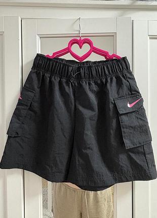 Чорні ткані шорти карго виглядають як модель від nike з яскраво-рожевим логотипом swoosh на бічній кишені.