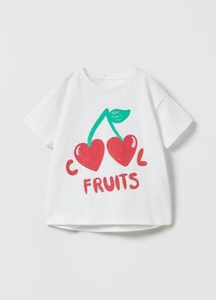 Белая футболка украшена ярким принтом с изображением вишеней и надписью 'cool fruits'