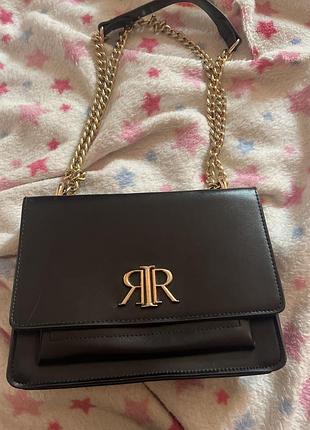 Чорна штучна шкіряна сумка через плече бренду river island із золотистою металевою фурнитурою та характерним логотипом ri на клапані