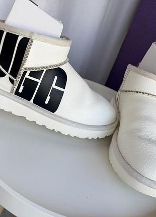 Білі шкіряні уггі моделі ugg classic ultra mini broken logo з великим чорним логотипом на боці.