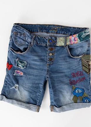 Оригінальні, жіночі, джинсові шорти desigual у блакитному кольорі. модель має декоративні вишивки та нашивки, потертості й рвані елементи спереду, яск