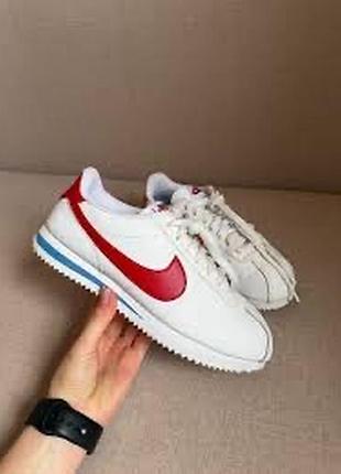 Классические кроссовки nike cortez белого цвета с красным логотипом-свушем и характерной синей полоской на подошве.