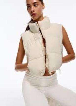 Укороченный дутый жилет bershka выполнен в молочно-белом цвете и дополнен высоким воротником-стойкой,