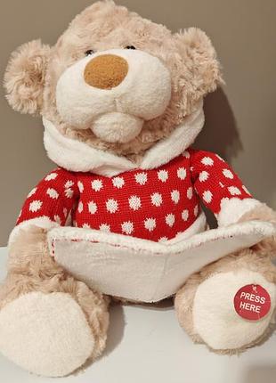 Интерактивная мягкая игрушка cuddle barn "storytime teddie", одетая в красный свитер с белым узором и держащая в лапках книжку