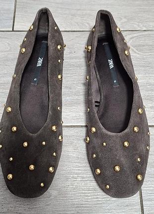 Женские замшевые балетки от бренда zara шоколадного цвета, украшенные круглыми золотистыми заклепками. обувь имеет круглый носок и плоскую подошву.