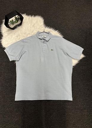 Світло-блакитне чоловіче поло бренду lacoste з коротким рукавом та фірмовим логотипом у вигляді зеленого крокодила на грудях.