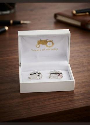 Серебристые запонки в форме трактора от норвежского бренда moods of norway, аккуратно упакованные в фирменную белую коробочку с логотипом