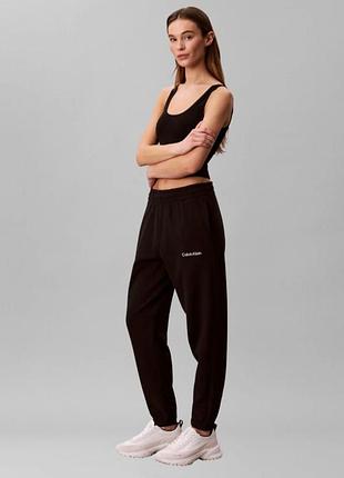 Черные спортивные штаны бренда calvin klein с фирменными надписями на поясе, бедре и лампасах.