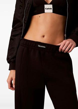 Черные спортивные штаны бренда calvin klein с фирменными надписями на поясе, бедре и лампасах.