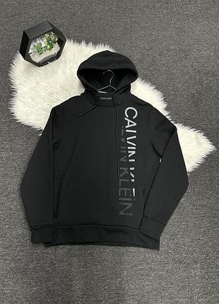Чорне чоловіче худі від бренду calvin klein з вертикальним контрастним логотипом на передній частині.