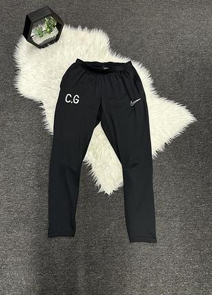 Чорні спортивні штани nike з білим логотипом swoosh та принтом «c.g» на правому стегні.