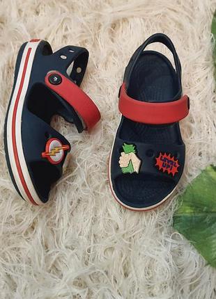 Сині дитячі сандалі бренду crocs з червоними ремінцями та декоративними значками-джибітсами