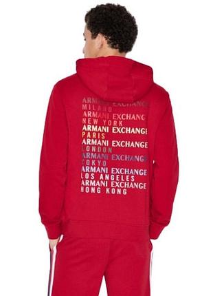Красный худи зипка с капюшоном от armani exchange с разноцветным принтом названий городов на спине и полосками на рукавах.