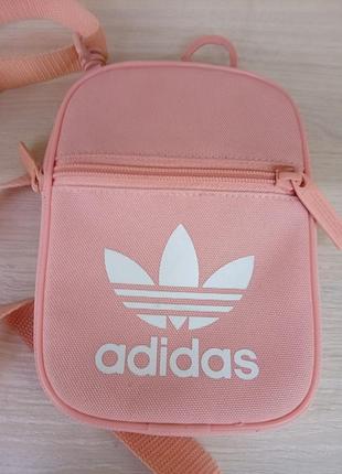 Рожева маленька сумка через плече моделі adidas adicolor classic festival bag з білим логотипом-трилисником adidas originals.