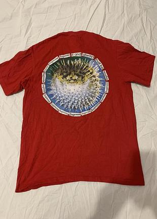 Червона футболка supreme blowfish tee з колекції ss23 із зображенням риби-фугу та круговим написом на спині.