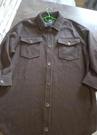 Коричневая куртка-рубашка с накладными карманами на пуговицах и мягкой фактурой ткани.