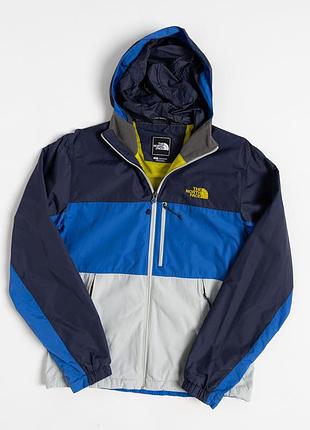 Чоловіча куртка the north face у поєднанні темно-синього, синього та світло-сірого кольорів. модель має капюшон, високий комір, центральну застібк